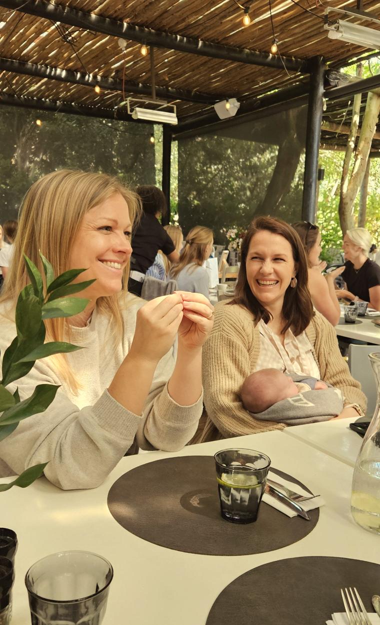 Two members laughing together at a Boss Moms meetup, one holding her baby
